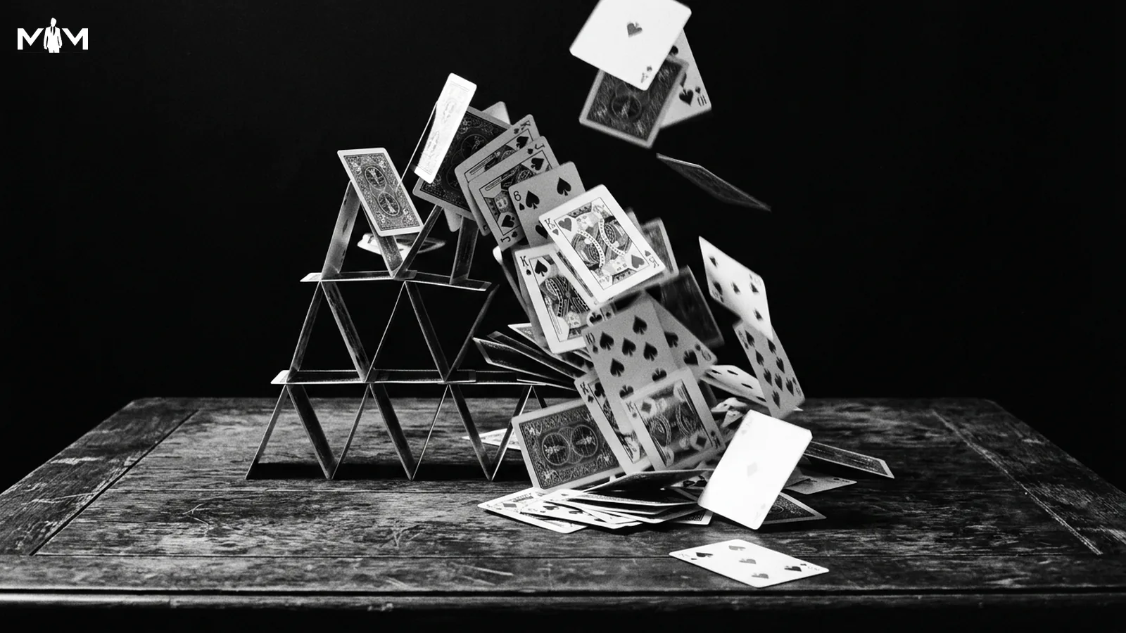 House of cards mid collapse on a bare wooden table dramatic directional side lighting dark